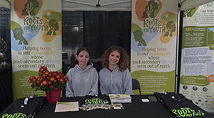 Two young adults sit at a table-top display at a Roots for Youth event.
